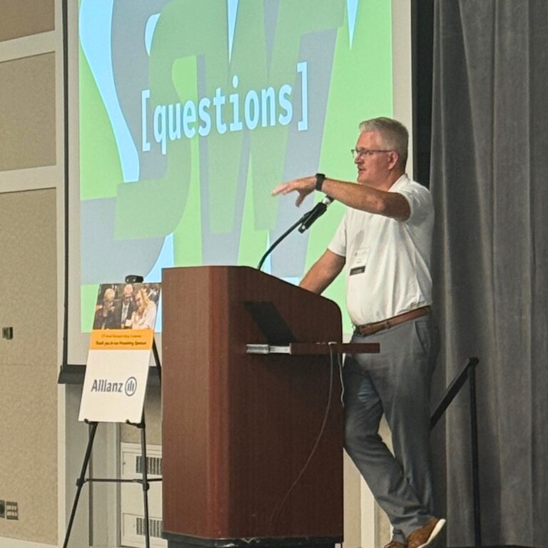 A man presenting on stage on front a large screen that says "questions."