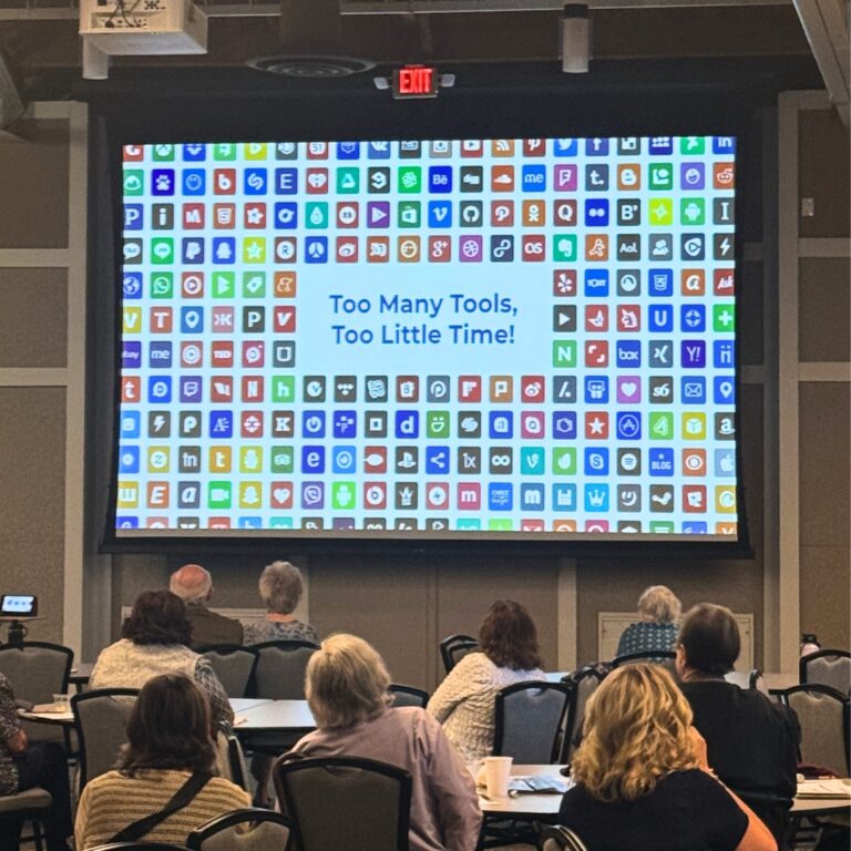 A photo of a projector screen with the words "Too many tools, too little time" written on it.