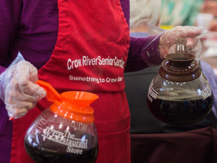 Someone serving coffee in an apron that says "Crow River Senior Center."
