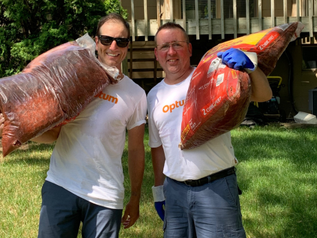Two men holding bags of mulch in a backyard.